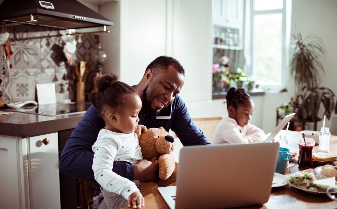 Father working at the kitchen table while holding his child.
