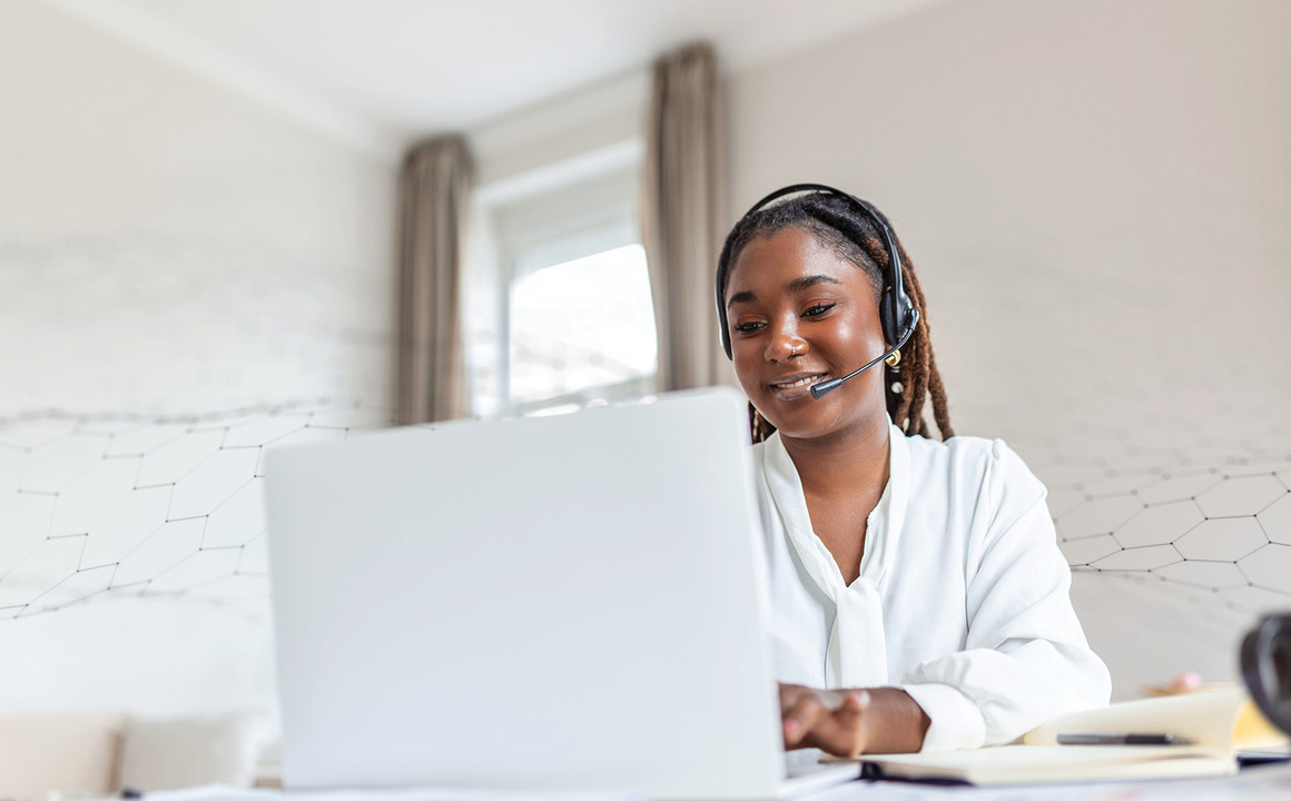 A woman wearing a headset, working on a laptop in a bright, modern room.