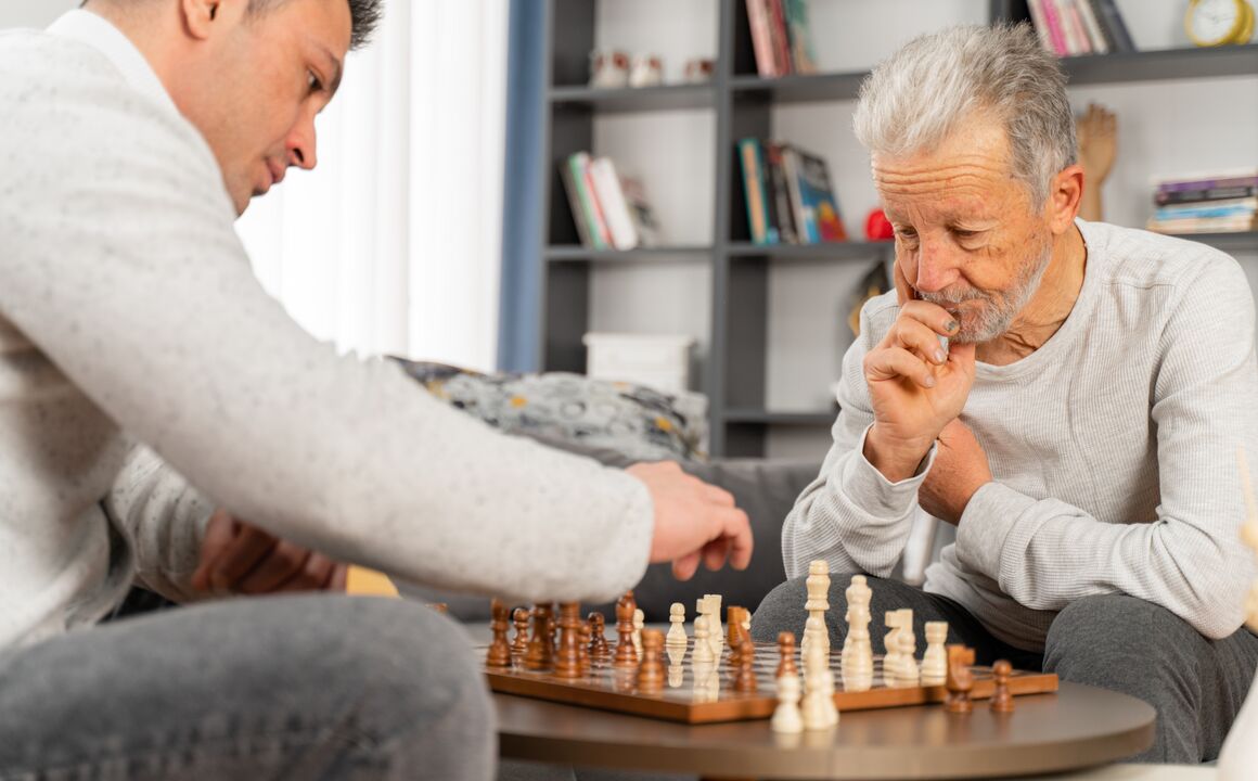 Older man plays chess with his son.