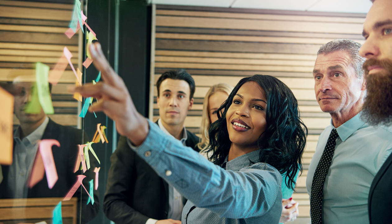 Female consultant points to sticky note while brainstorming with government clients