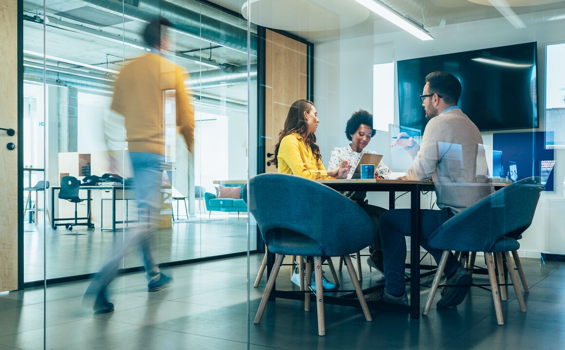Colleagues in a business meeting while a man walks down the hallway.