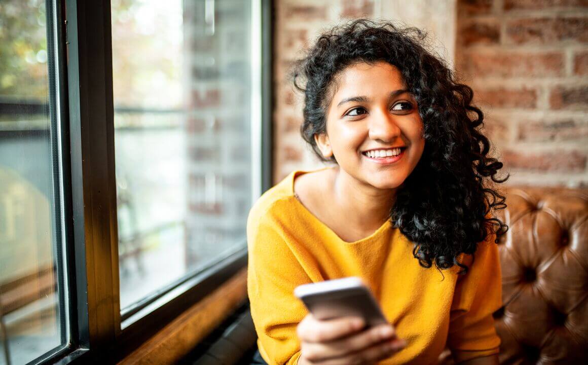 Young woman smiling holding cell phone.